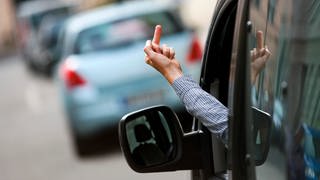 Ein Mann hält den ausgestreckten Mittelfinger aus dem Seitenfenster seines Autos. Aggressionen im Straßenverkehr scheinen sich seit der Corona-Pandemie zu häufen, so kommt es zumindest vielen Menschen vor.