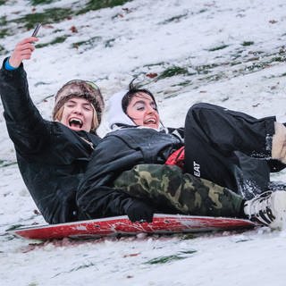 Spaß im Schnee: Ein jungen Paar rutscht einen Hügel hinunter 