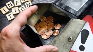 Hand öffnet Portemonnaie mit Kleingeld, Schriftzug Inflation und Gefahrenschild