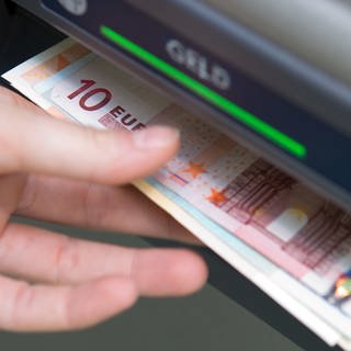 Eine Hand greift nach Geldscheinen, die aus einem Geldautomaten ausgeworfen wurden. 