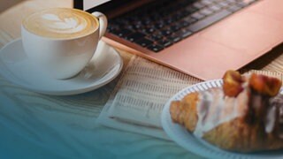 Ein Croissant und ein Café stehen auf einem Tisch vor einem Laptop