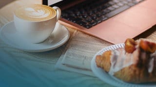 Ein Croissant und ein Café stehen auf einem Tisch vor einem Laptop