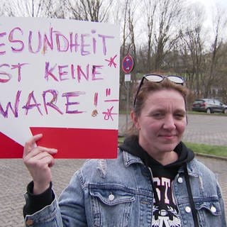 Frau hält Demoschild mit Aufschrift: 'Gesundheit ist keine Ware' hoch