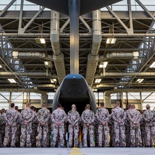 Soldaten der Bundeswehr sind von hinten zu sehen. Vor ihnen steht ein Flugzeug. 