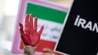 Die rot bemalte Hand einer Demonstrantin erhebt sich zwischen Plakaten während einer Demonstration vor dem iranischen Konsulat. Nach dem Tod einer 22-jährigen in Teheran kommt es weltweit zu Protesten und Solidaritätskundgebungen.