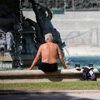 Ein Mann steckt bei heißen Temperaturen seine Füße in einen Brunnen, um sich abzukühlen