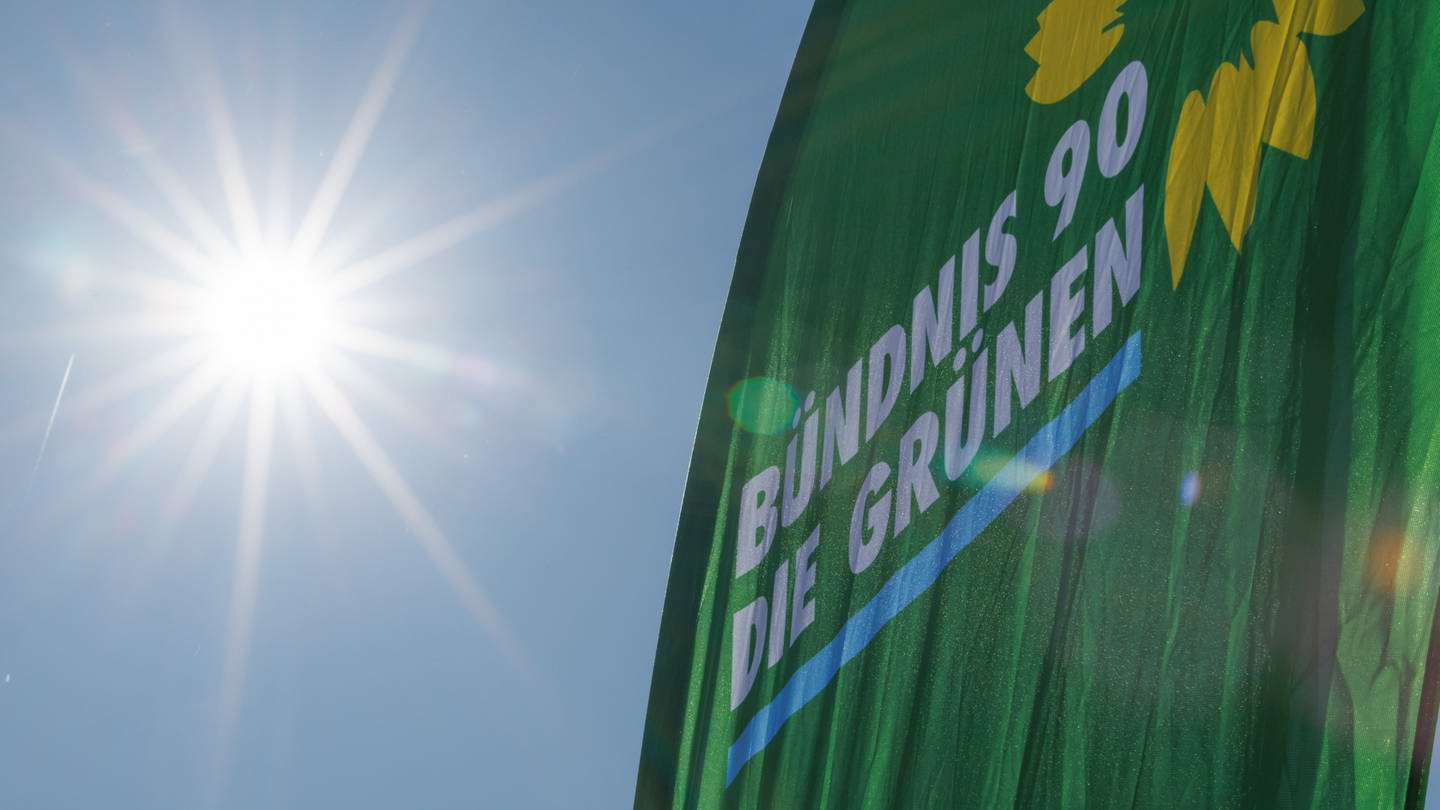 Eine Fahne der Partei Bündnis 90/Die Grünen weht neben der strahlenden Sonne