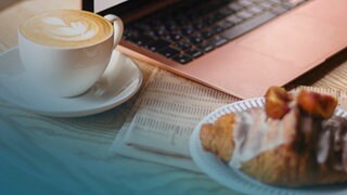 Ein Croissant und ein Café stehen auf einem Tisch vor einem Laptop