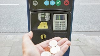 Parkscheinautomat und Hand mit Münzen