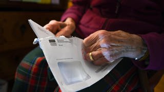 Eine alte Frau öffnet einen Brief der Deutschen Rentenversicherung.