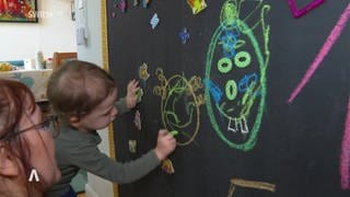 Kind malt mit bunter Kreide auf eine Tafel