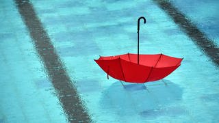Man sieht einen roten Regenschirm im Freibad-Becken