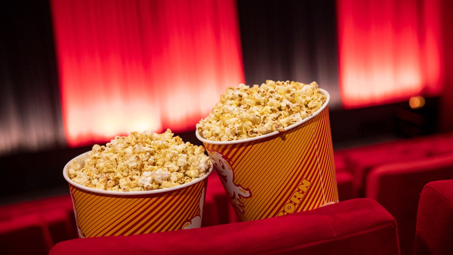 Popcorn steht zwischen den Sitzreihen in einem Kino.