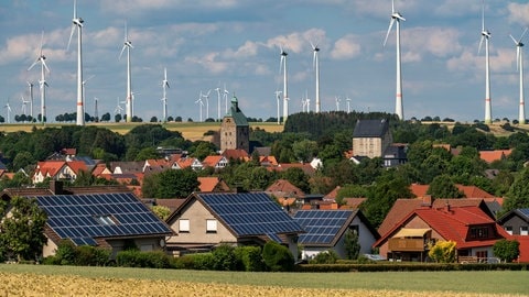 Solaranlagen sind auf Hausdächern installiert. Im Hintergrund drehen sich Windräder.