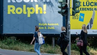 Frauen gehen an einem Plakat mit der Aufschrift "Rock 'n' Rolph!" vorbei, das Teil einer Mobilitäts-Kampagne der Landesregierung war.