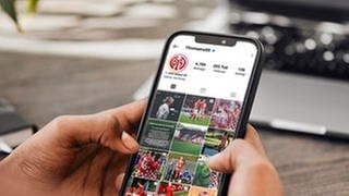 Eine Hand hält ein Handy mit dem Instagram des Fußballligisten Mainz 05.