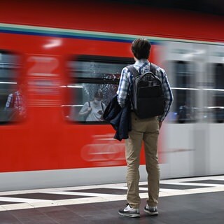 Zwei Menschen stehen an einem Bahnsteig, als ein Zug einfährt.