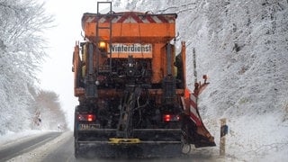 Ein Einsatzfahrzeug des Winterdienstes räumt Schnee von einer Straße in RLP und streut Salz. 