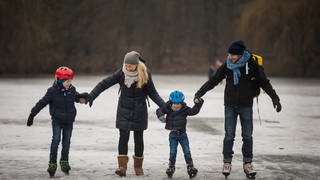 Eine Familie beim gemeinsamen Eislaufen auf einem zugefrorenen Weiher