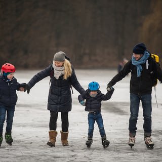 Eine Familie beim gemeinsamen Eislaufen auf einem zugefrorenen Weiher