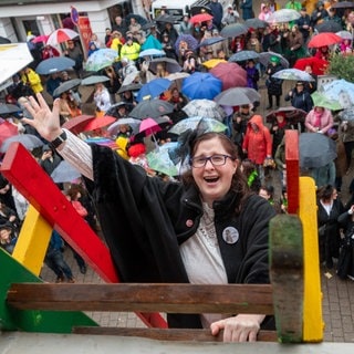 Die Wittlicher Möhne Clara Boor winkt auf einer Leiter stehend in die Narrenschar. 