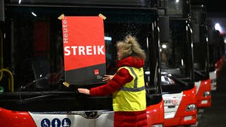 Eine Mitarbeiterin klebt ein Plakat mit der Aufschrift "Streik" auf die Frontscheibe eines Busses. 