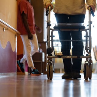 Ein Bewohner eines Pflegeheims geht mit einem Rollator einen Gang entlang.