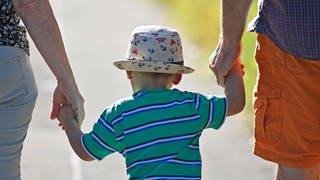 Mutter und Vater gehen mit Kleinkind an der Hand spazieren - am 15. Mai ist Internationaler Tag der Familie.