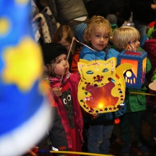 Kinder halten ihre bunten, selbstgebastelten Laternen bei einem Martinsumzug fest.