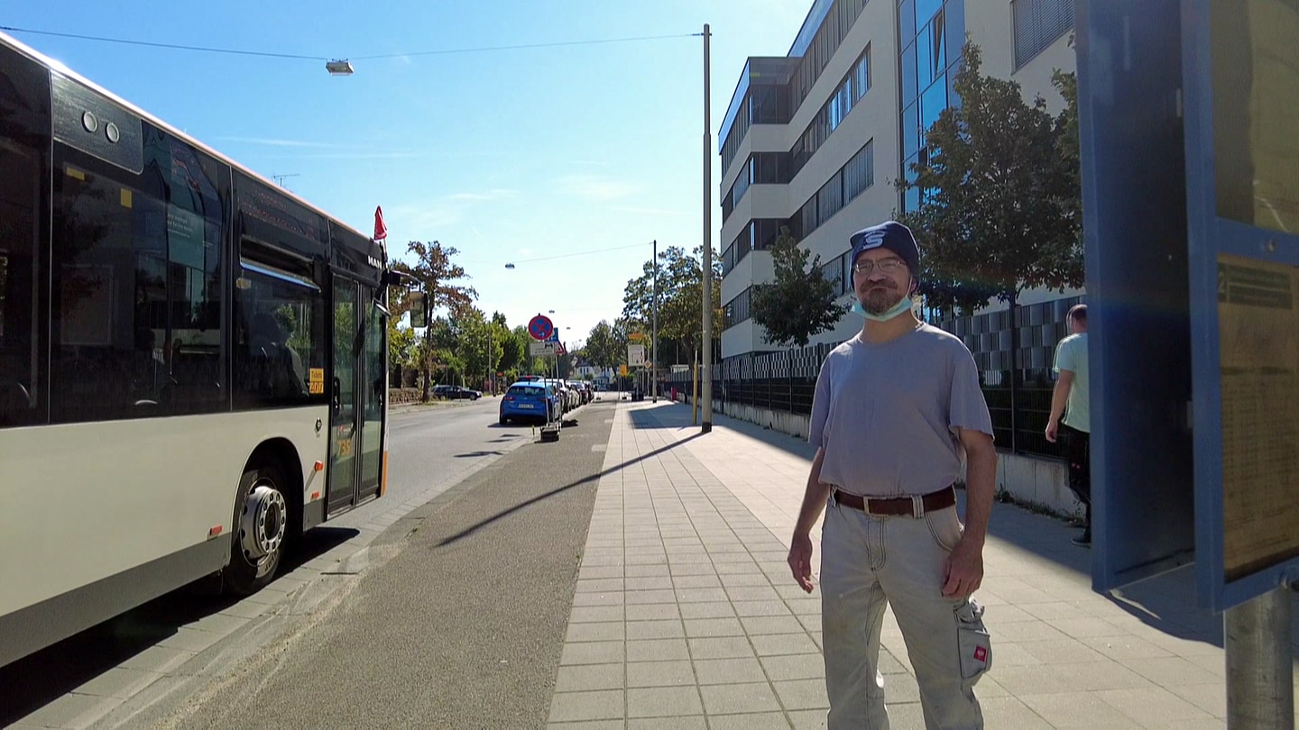 Der Bewohner des Thaddäusheims Mainz, Lorenz Franco Siegfried, steht an einer Bushaltestelle. Ein Bus hält links neben ihm.