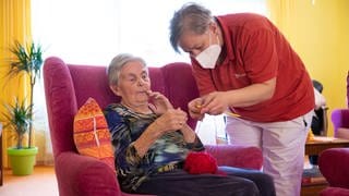 Eine Betreuerin hilft im Altenheim einer Bewohnerin in einer Wohngruppe beim Stricken.
