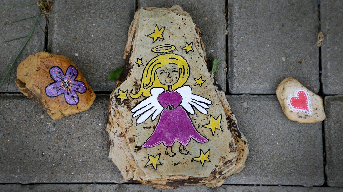 Ein mit einem Engel bemalter Stein liegt auf dem Boden