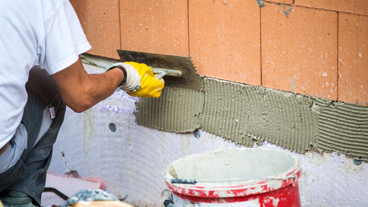 Ein Maurer trägt auf einer Baustelle Klebemörtel auf eine Wand auf.