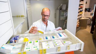 Ein Apotheker steht hinter einer ausgezogenen Schrankschublade und hält ein Medikament in der Hand. Auch in Rheinland-Pfalz haben Apotheken momentan Lieferengpässe bei manchen Medikamenten wie beispielsweise dem Antibiotikum Amoxicillin.