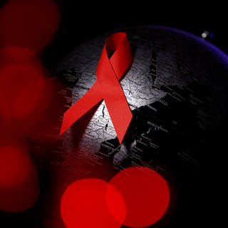 Es ist das für AIDS bekannte Symbol der roten Schleife zu sehen, auf einem schwarzen Hintergrund.