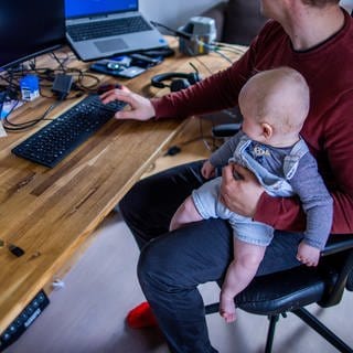 Ein junger Vater sitzt im Homeoffice mit seinem kleinen Sohn im Arbeitszimmer. In den Stellenanzeigen bieten immer mehr Arbeitgeber die Möglichkeit von Homeoffice an. Das ist das Ergebnis einer Bertelsmann Studie. 