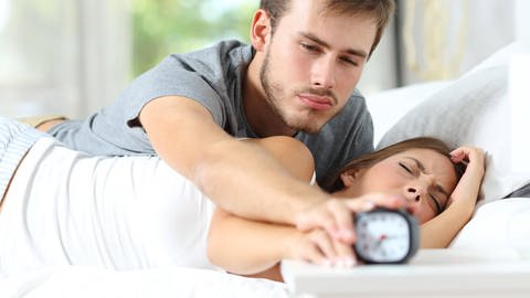 Paar im Bett: Verschlafener Mann haut Wecker der Frau aus.
