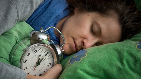 Schlafende Frau hält Wecker in der Hand.