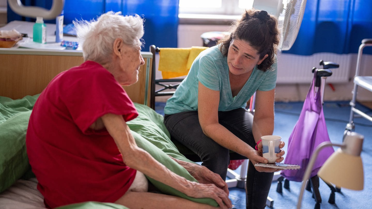 Eine Pflegerin hört einer pflegebedürftigen Seniorin beim Hausbesuch zu