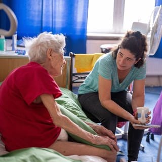 Eine Pflegerin hört einer pflegebedürftigen Seniorin beim Hausbesuch zu