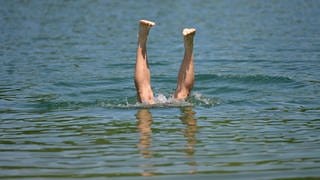 Ein Mann taucht kopfüber in einen Badesee, man sieht die nach oben streckten Beine