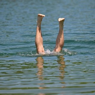 Ein Mann taucht kopfüber in einen Badesee, man sieht die nach oben streckten Beine