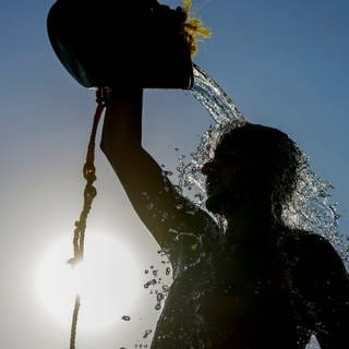 Ein Mann kühlt sich mit einem Eimer Wasser ab. Am Wochenende werden in RLP über 30 Grad erwartet.