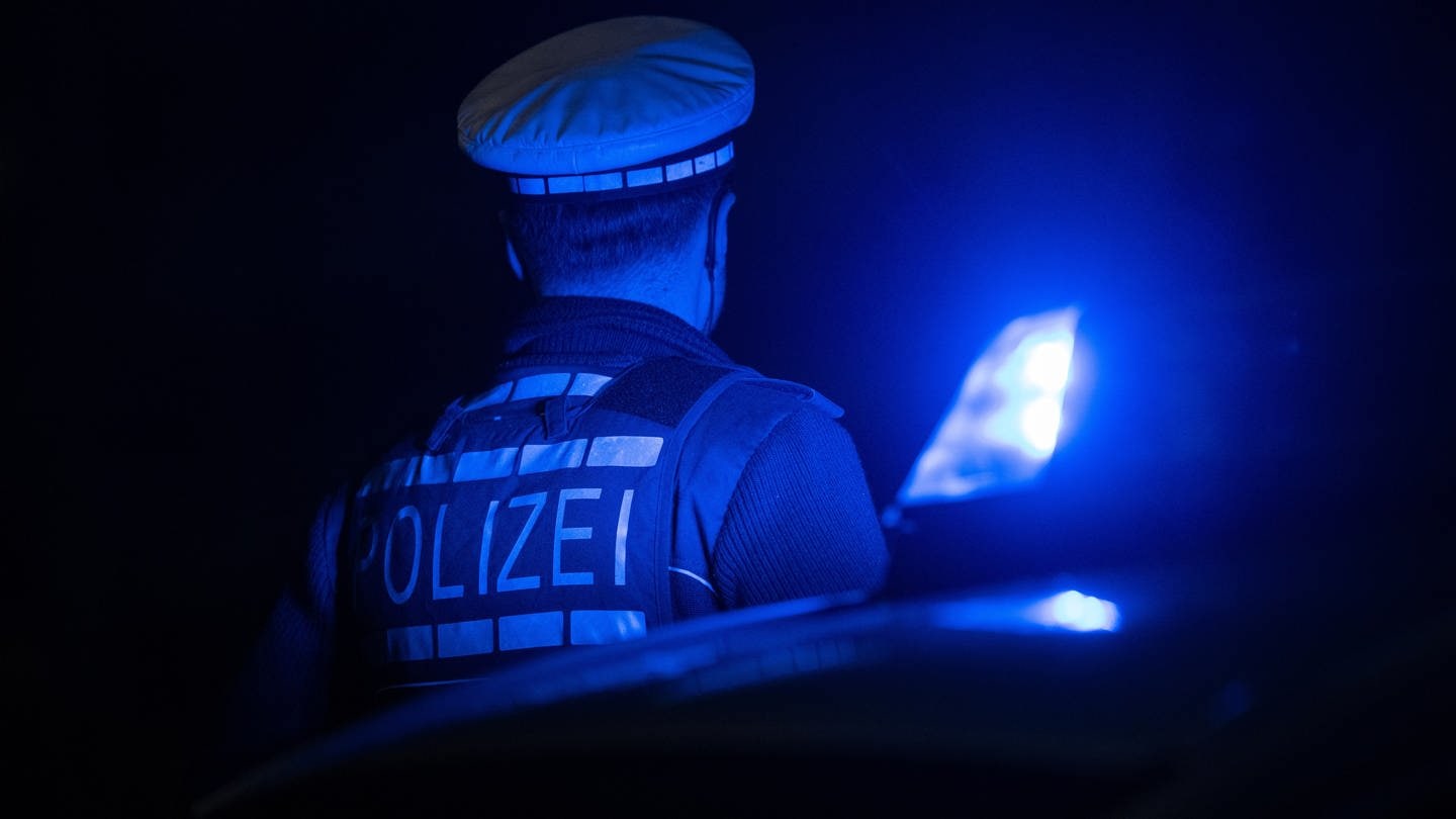 Ein Polizist steht in der Dunkelheit neben seinem Streifenwagen. In Ludwigshafen ist in der Nacht zu Montag ein Mann bei einem Unfall gestorben.