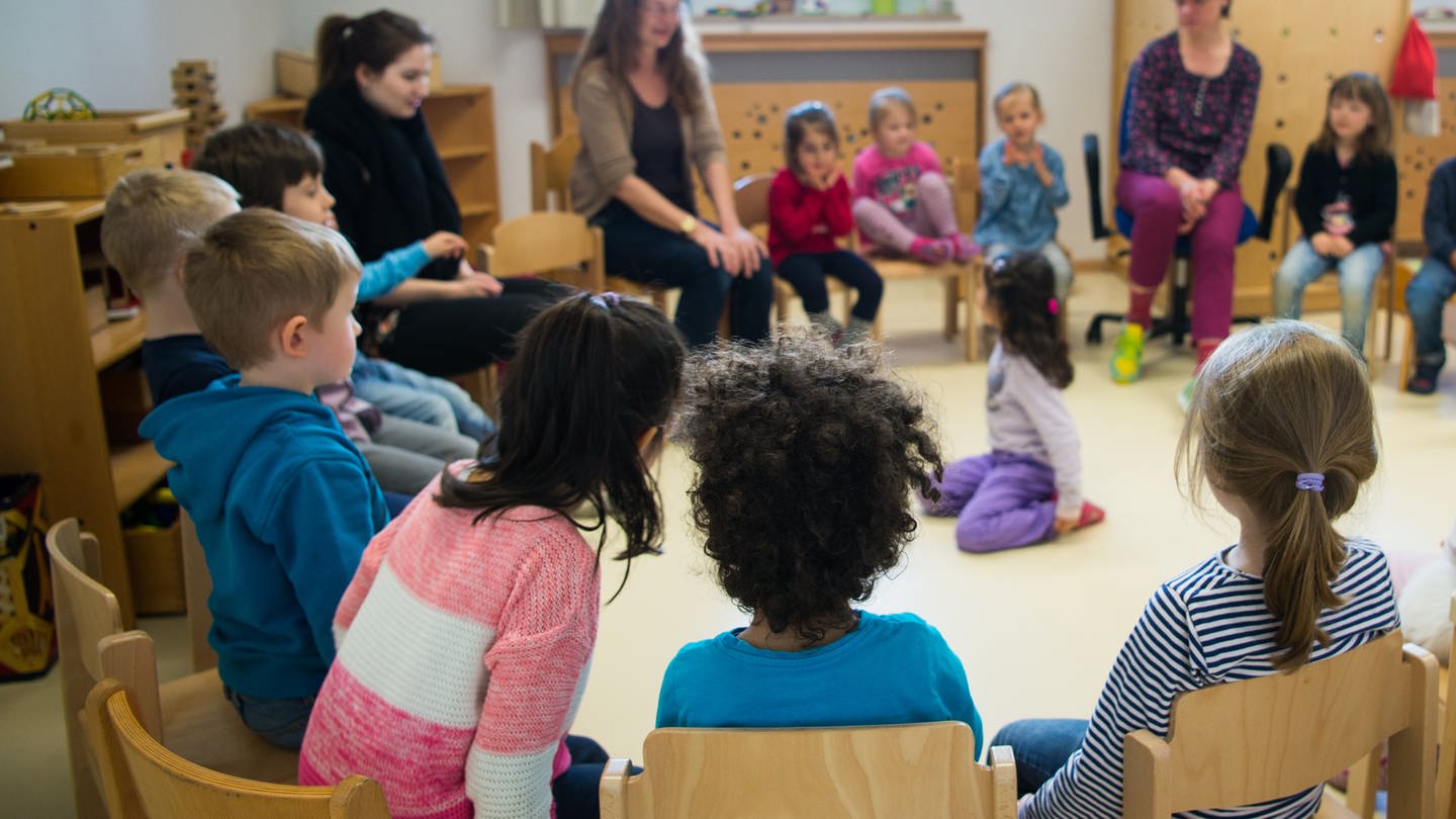 Kinder und Erzieherinnen sitzen in einer Kita im Kreis.