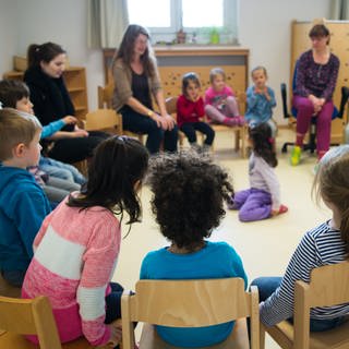 Kinder und Erzieherinnen sitzen in einer Kita im Kreis. 