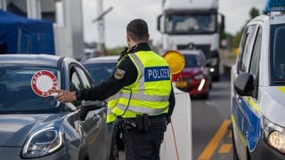 Ein Polizeibeamter kontrolliert an einer Landesgrenze einen Autofahrer (Symbolbild).