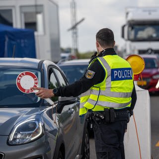 Ein Polizeibeamter kontrolliert an einer Landesgrenze einen Autofahrer (Symbolbild).