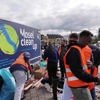 Personen mit Warnwesten stehen vor einem Schild mit der Aufschrift "Mosel clean up"