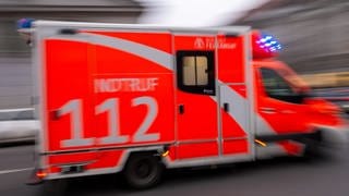 Ein rot-weißer Krankenwagen der Feuerwehr mit der Notrufnummer 112 fährt mit eingeschaltetem Blaulicht schnell durch die Stadt. 